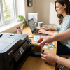 A person is inserting the Balloon Brand Brother LC3013XL Yellow Ink Cartridge into a Brother printer in a bright home office.