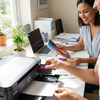 A couple in a sunny home office. A man is installing the Balloon Brand LC404 magenta ink cartridge into a Brother printer while a woman smiles, looking at a vibrant printed photo.