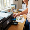 A person's hand inserts the cyan LC103C ink cartridge into a Brother printer in a sunlit home office.
